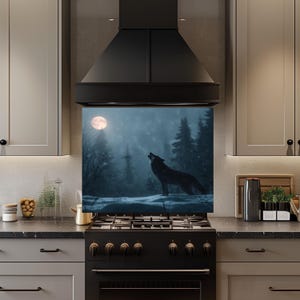 Puede incluir: Un protector contra salpicaduras de cocina con una imagen de un lobo negro aullando a la luna en un bosque nevado. La obra de arte está enmarcada por una campana extractora y una estufa negras. La paleta de colores es principalmente negra, blanca y gris.