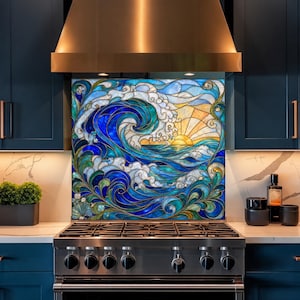 Op de afbeelding: Een decoratief achterwandpaneel met een ontwerp in glas-in-loodstijl van een grote oceaangolf die breekt onder een opkomende zon. Het kunstwerk gebruikt levendige tinten blauw, groenblauw en goud, met ingewikkelde lijnen die het water vormen.