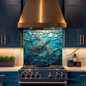 May include: A kitchen backsplash featuring a mosaic design with three sea turtles in shades of teal, turquoise, and gold. The turtles are set against a background of broken glass-like tiles in varying shades of blue. The backsplash is installed above a stainless steel stove.
