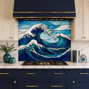 Könnte beinhalten: Ein Küchenrückwand-Design aus Buntglas, das große, brechende Meereswellen in verschiedenen Blau- und Weißtönen zeigt. Das Kunstwerk befindet sich hinter einem schwarzen Gasherd und ist von dunkelblauen Schränken sowie einer Dunstabzugshaube umrahmt.