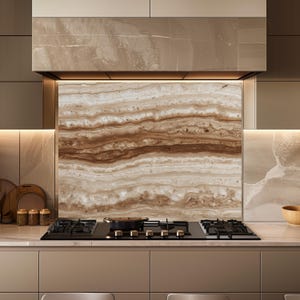 May include: A modern kitchen design featuring a black gas cooktop with a pan, set against a backsplash with a layered brown and beige stone pattern. The cabinetry is a neutral beige color, and the overall aesthetic is sleek and contemporary.