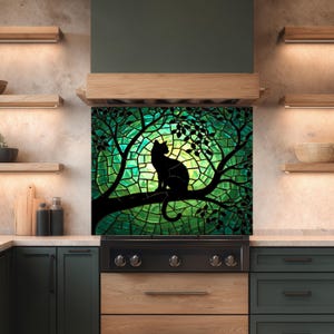 Puede incluir: Silueta negra de un gato posado en una rama, sobre un fondo de estilo vidriera en tonos verdes y amarillos. La obra está enmarcada por un entorno de cocina verde oscuro y negro, con estantes de madera y una estufa.