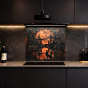 Puede incluir: Una obra de arte mural en negro y naranja que representa un lobo aullando a la luna llena sobre un lago y árboles. La obra de arte está montada sobre una placa de cocina negra en un entorno de cocina moderno.