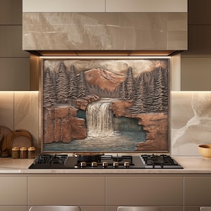 May include: A decorative kitchen backsplash featuring a detailed relief of a waterfall scene with trees and mountains. The artwork is in shades of brown and copper, creating a natural, rustic aesthetic. The backsplash is installed above a black stovetop.