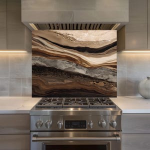 Puede incluir: Salpicadero de cocina decorativo con un diseño abstracto en capas en tonos marrón, beige y gris. Se instala sobre una cocina de gas de acero inoxidable, creando una estética de cocina moderna.