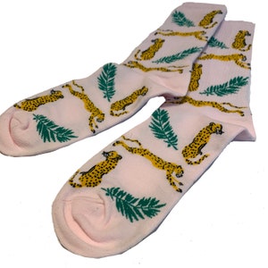 May include: A pair of pink socks with a pattern of yellow cheetahs and green palm leaves.
