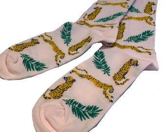 May include: A pair of pink socks with a pattern of yellow cheetahs and green palm leaves.