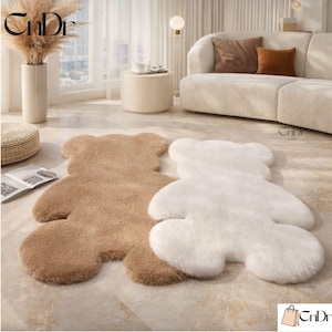May include: Two plush bear-shaped rugs. One rug is a light brown color, and the other is white. The rugs are on a tiled floor. The rugs are in a living room setting with a sofa and side table.