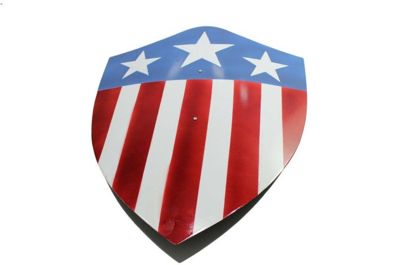 Op de afbeelding: Een schildvormig object met een patriottisch ontwerp. Het bovenste gedeelte is blauw met drie witte sterren, terwijl het onderste gedeelte afwisselend rode en witte strepen heeft. Het schild heeft een glanzende afwerking en een puntige onderkant.