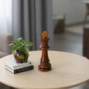 Peut inclure: Un roi d'échecs en bois est posé sur une table ronde en bois clair. Une petite plante en pot et deux livres sont également sur la table. La table a un seul pied en bois et se trouve dans une pièce aux tons neutres.