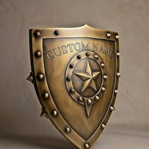 Peut inclure: Un bouclier de couleur bronze avec le texte "CUSTOM NAME" en haut. Le bouclier a une étoile au centre et est entouré de rivets et de pointes. L'objet est sur le thème médiéval.