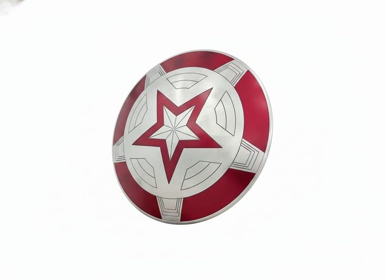 May include: A silver and red shield with a large white star in the center. The shield has a circular design with a red outer ring and a silver inner section. The star is outlined in red.