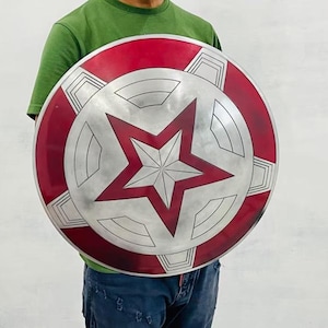 May include: A round shield with a red and silver design. The outer rim is red, with silver geometric shapes. The center features a large, red, five-pointed star on a silver background. A classic superhero accessory.