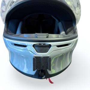 Peut inclure: Casque de moto bleu clair avec une visi&egrave;re transparente. L'int&eacute;rieur du casque est noir et il y a un support de montage noir &agrave; l'avant. Une petite languette rouge pend en bas.