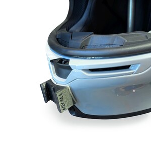 Peut inclure: Gros plan sur un casque blanc et noir avec un accessoire noir fix&eacute; sur le c&ocirc;t&eacute;. L'accessoire porte l'inscription "ASV RACE". Le casque est con&ccedil;u pour la s&eacute;curit&eacute; et la protection.