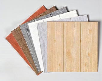 Puede incluir: Un conjunto de paneles murales de espuma con aspecto de madera en varios colores, incluyendo marrón claro, gris, blanco y marrón rojizo. Los paneles están dispuestos en forma de abanico, mostrando sus diferentes patrones y texturas de vetas de madera.