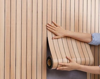 Puede incluir: Un rollo de papel pintado de color madera marrón claro con líneas negras verticales se está aplicando a una pared. Una persona está desenrollando el papel pintado. La pared también está cubierta con el mismo papel pintado.