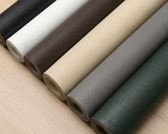 Puede incluir: Una colección de siete rollos de material de piel sintética texturizada en varios colores, incluyendo negro, blanco, marrón oscuro, beige, gris claro, gris medio y verde oscuro, dispuestos en fila diagonal sobre madera clara.