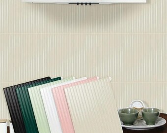 Puede incluir: Una colección de seis baldosas decorativas cuadradas y acanaladas en varios colores: negro, verde oscuro, verde claro, blanco, rosa y beige. Las baldosas están dispuestas en forma de abanico, con una campana extractora blanca y una pared crema con líneas verticales en el fondo.