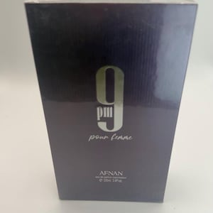 Puede incluir: Caja de perfume gris oscuro con el texto "9 PM pour femme" en blanco. La marca "AFNAN" est&aacute; impresa debajo, junto con el volumen: 100 ml, 3,4 fl oz.