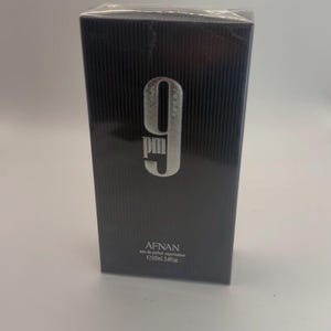 Puede incluir: Una caja de perfume negra rectangular con líneas verticales. La caja presenta el texto plateado "9 pm" y la marca "AFNAN". La caja contiene 100 ml de perfume.