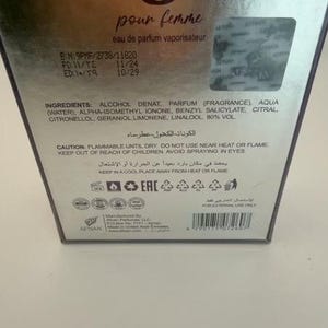 Puede incluir: Caja de perfume plateada con las palabras "pour femme" en cursiva. La caja incluye informaci&oacute;n sobre ingredientes y advertencias de seguridad. El producto es un eau de parfum vaporisateur.