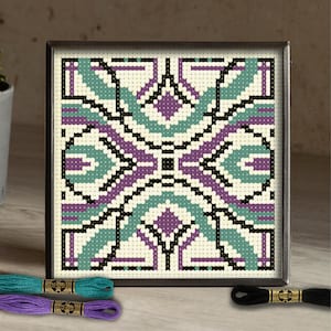 Peut inclure: Une œuvre d'art au point de croix encadrée avec un motif géométrique en turquoise, violet, noir et crème. L'œuvre est présentée dans un cadre foncé. Trois échevettes de fil à broder turquoise, violet et noir sont au premier plan.