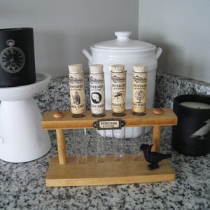 May include: A decorative Halloween-themed display featuring potion bottles, candles, and a white pedestal. The potion bottles are in a wooden rack, and the candles are black with white designs. A white ceramic jar is in the background.