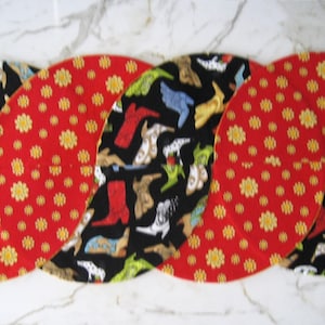 May include: Four oval-shaped placemats arranged in a braid pattern. The placemats alternate between a red background with yellow flowers and a black background with colorful cowboy boots. A decorative table setting.