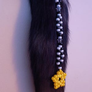May include: A dark gray and white faux fur tail with a beaded accent. The beaded strand features alternating black and white beads, with a yellow star-shaped bead cluster at the end. The tail is a unique accessory.