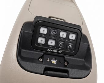 May include: A beige overhead console featuring a black Auxbeam switch panel with six buttons. The buttons include icons for a fish box, grille, and amber lights. The panel is integrated into the plastic housing, which also contains a small light.