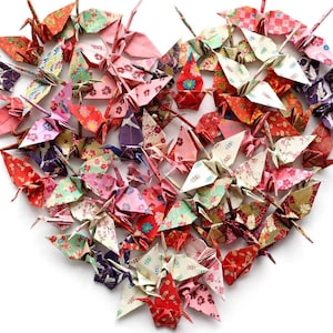 May include: A collection of numerous origami paper cranes arranged in the shape of a heart. The cranes are crafted from various patterned papers featuring floral, geometric, and traditional motifs in shades of red, pink, white, and purple.
