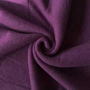 May include: A deep purple fabric with a soft, fuzzy texture. The material is gathered in the center, creating natural folds and shadows that highlight the rich, solid color and the dense, matte surface of the textile throughout the frame.
