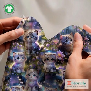 Può includere: Tessuto con un motivo ripetuto di adorabili gattini dei cartoni animati con occhi blu, ambientati in un paesaggio floreale e stellato stravagante. Il tessuto è tenuto in mano, mostrando i dettagli del design e il logo "Fabricly".