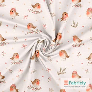 May include: A white fabric featuring a repeating pattern of small brown robins with red chests, some wearing pink knit hats or scarves. The design includes sprigs of red berries, pine needles, and small pink bows scattered across the surface.