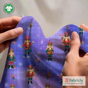 Puede incluir: Una muestra de tela con un patrón repetido de cascanueces de juguete con uniformes rojos, verdes y azules sobre un fondo de cuadros morados. La tela tiene el logo "Organic Textile Standard GOTS" y el logo "Fabricly".