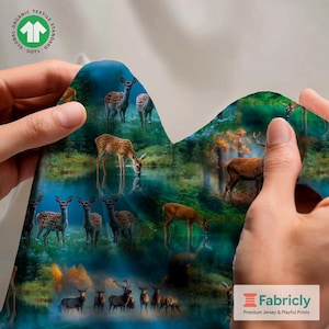 Könnte beinhalten: Stoffmuster mit einer Waldszene mit Hirschen in der Nähe eines Sees. Der Stoff hat eine blaue und grüne Farbpalette, mit Hirschen in Brauntönen. Der Stoff wird hochgehalten, um das Design zu zeigen. Das Fabricly-Logo ist sichtbar.