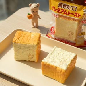 May include: Two square-shaped, toy bread slices with a chef logo are on a white tray. One slice has a light-colored top, the other has a white top. A small bear figurine holds a small orange fruit.