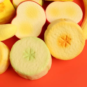 Puede incluir: Vista aérea de varias rodajas de fruta sobre una superficie roja. Las rodajas incluyen rodajas de manzana amarillas y verdes, y una rodaja de plátano amarilla. Las rodajas de manzana tienen un diseño en forma de estrella en el centro.