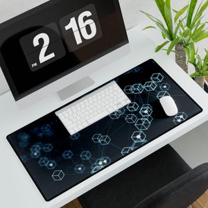 Può includere: Un tappetino da scrivania rettangolare nero con un design a cubo geometrico in azzurro. Una tastiera e un mouse bianchi sono posizionati sul tappetino. Un monitor di computer mostra l'ora 14:16.