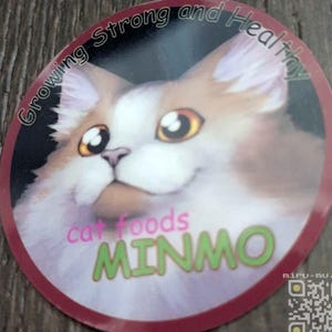 May include: A round sticker featuring a cartoon cat with orange and white fur, large eyes, and a smiling expression. The sticker has the text "Growing Strong and Healthy" and "cat foods MINMO" in pink and green, respectively. A QR code and website address are also visible.