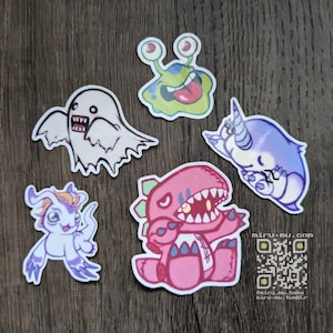 May include: A collection of five colorful cartoon stickers featuring various monster-like characters. The stickers include a ghost, a creature with large eyes and a tongue, a narwhal, a winged creature, and a dinosaur-like monster. The stickers are on a wooden surface.