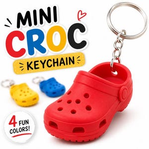 Puede incluir: Un llavero mini Croc rojo con un llavero plateado. La imagen también muestra llaveros mini Croc amarillos y azules. El texto en la imagen dice "MINI CROC KEYCHAIN" y "4 FUN COLORS!"