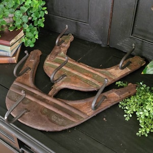 May include: Two rustic wooden coat hooks with metal hooks. The hooks are shaped like a horseshoe and have a distressed, weathered finish. The hooks are mounted on a dark wooden surface.