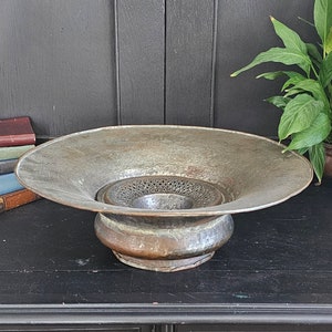 May include: A large, antique, copper-colored metal bowl with a decorative, perforated metal insert. The bowl has a wide, flared rim and a rounded base.