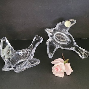 May include: Two clear glass bird-shaped dishes. The dishes are made of crystal and have a delicate, elegant design. One dish is flying with its wings spread out, while the other is perched with its wings folded.