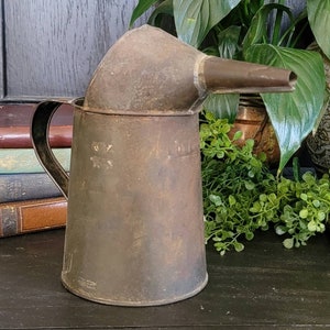May include: A vintage metal watering can with a spout, showing signs of wear and rust. The can is brown and has a handle.