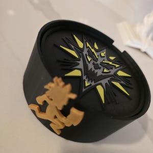 May include: Black round coaster featuring a yellow and grey explosion graphic and a running figure with an axe. The coaster is made of a durable material and is designed to protect surfaces from drink condensation.