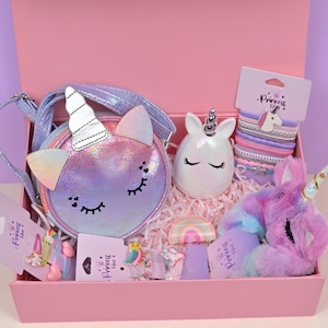 May include: A pink gift box filled with unicorn-themed accessories. Includes a pastel-colored unicorn purse, a white unicorn-shaped container, hair ties, hair clips, and a plush unicorn. The box is lined with pink paper.