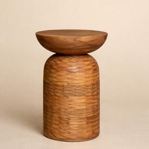 Puede incluir: Una mesa auxiliar de madera con un diseño único. La mesa presenta una parte superior redonda y una base cilíndrica, ambas hechas de madera marrón claro. La base tiene un aspecto texturizado y en capas. La mesa es una pieza decorativa.